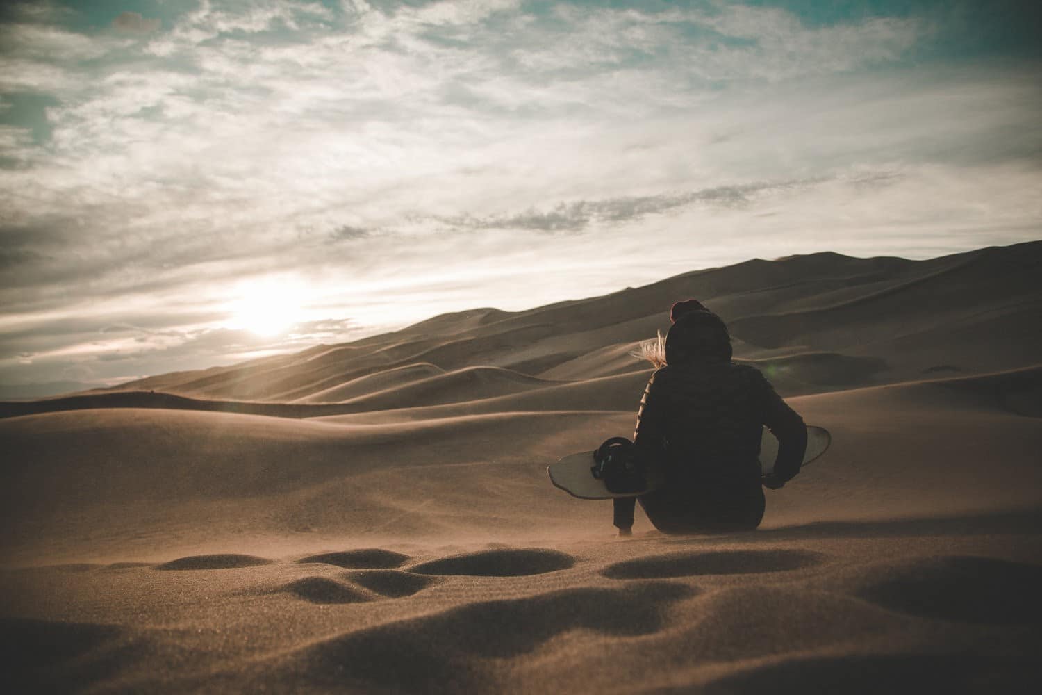 Woman sits with sandboard at the Great Sand Dunes 