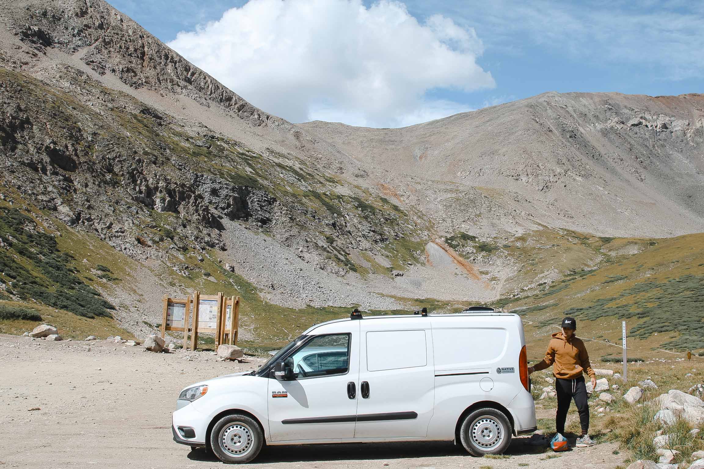 Man opening the back of a small campervan in the mountains