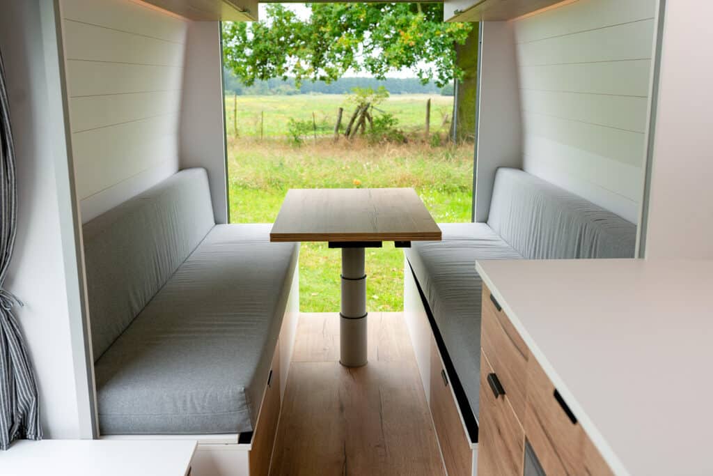 Table and bench dining setup in The Biggie campervan with open doors overlooking a field