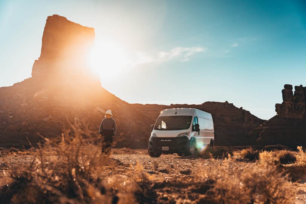 Vanlifer standing outside The Biggie campervan surrounded by desert red rocks
